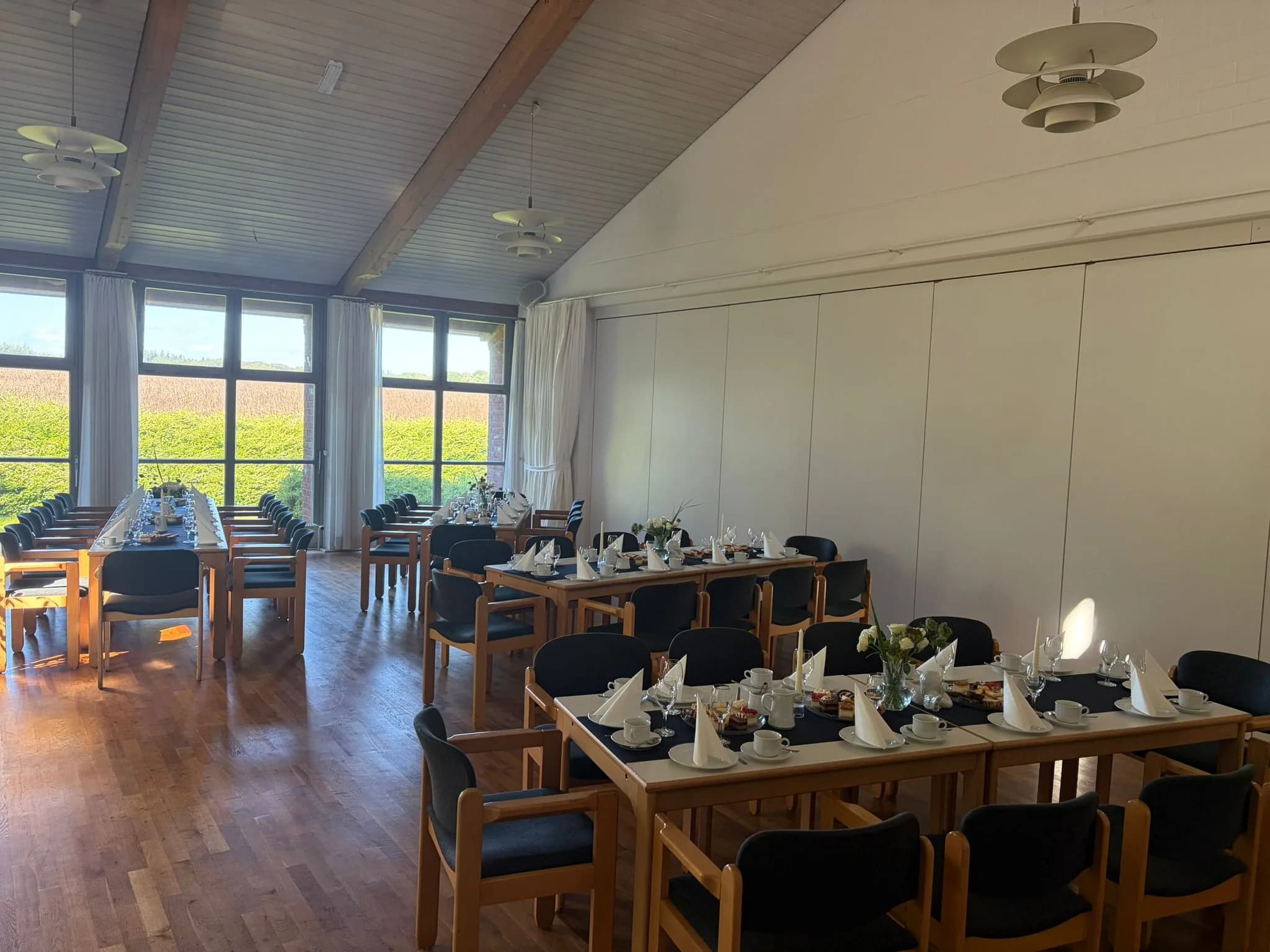 Heller Saal mit Fensterfront auf ein blühendes Rapsfeld, davor eine weiß eingedeckte Tafel