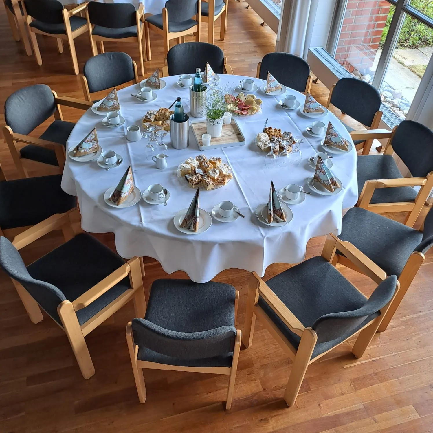 Runde Kaffeetafel mit Kuchen, Tassen und gefalteten Servietten